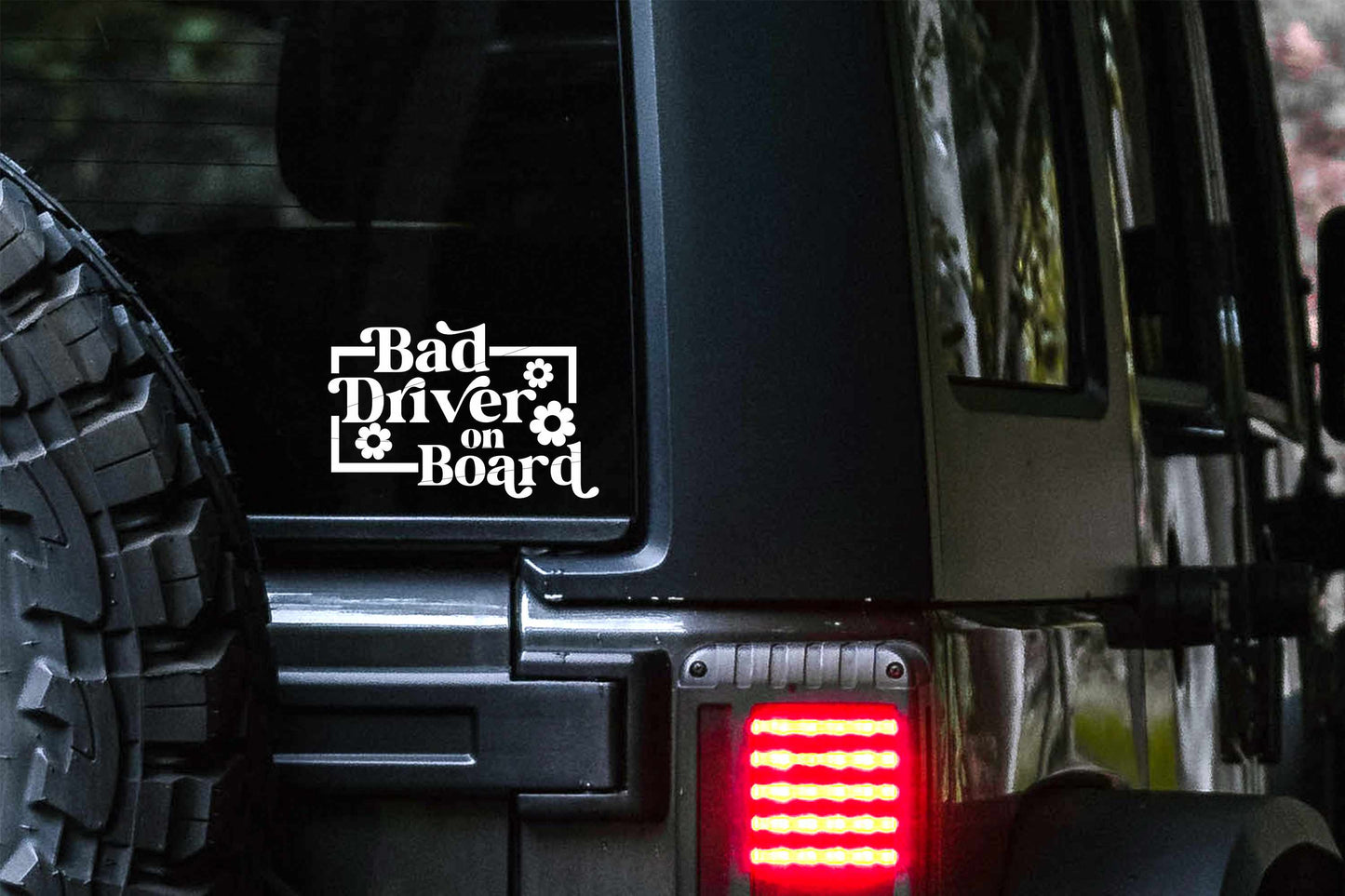 A retro flower design vinyl car decal that reads 'Bad driver on board' and sticks to the glass of your vehicle window.